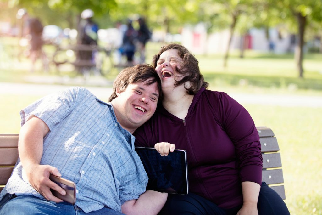 Two people with disability laughing on a park bench
