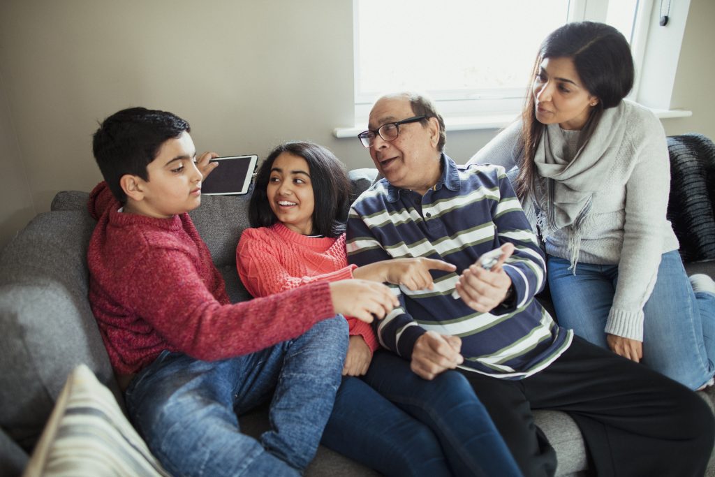 grandfather sitting down on a sofa with his two grandchildren and his daughter