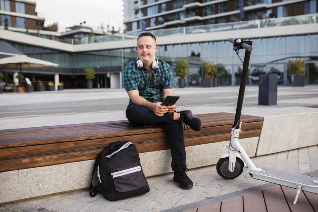 Young man student with Down syndrome riding an electric scooter holding tablet